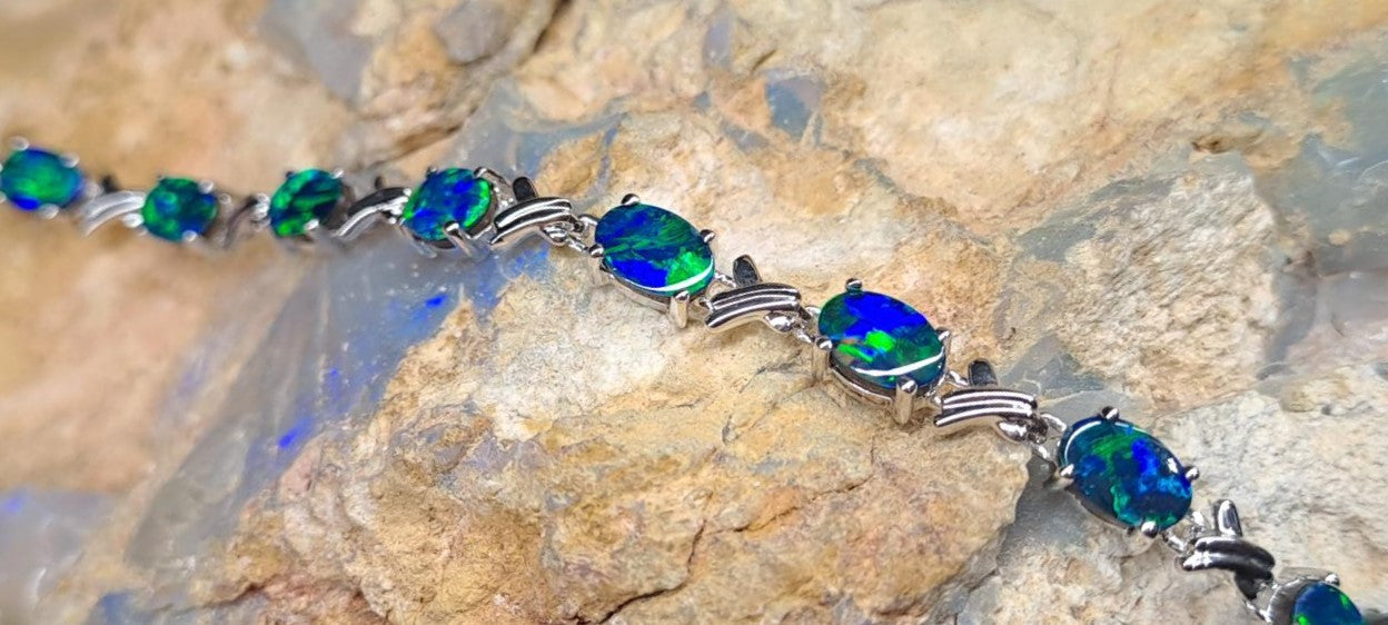 A bracelet of individual blue-green opals set in silver are laid across a piece of rock